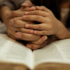 a kid reading the holy bible with guide by parents